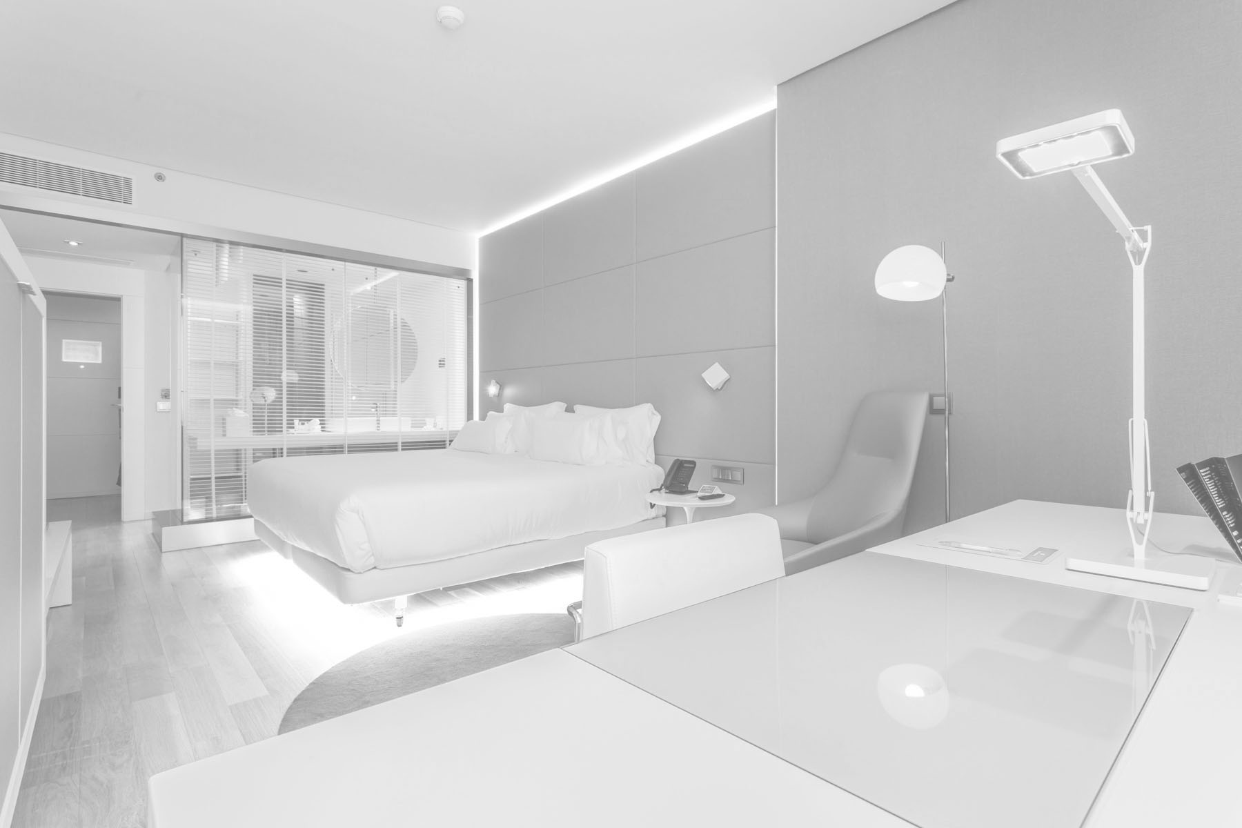 Habitación de hotel de 4 estrellas con el escritorio en primer término, una gran cama y un baño separado por una cristalera semi transparente