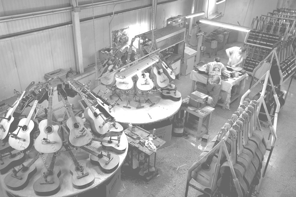 Proceso de producción de guitarras españolas, con numerosas guitarras secándose y un par de técnicos trabajando. 