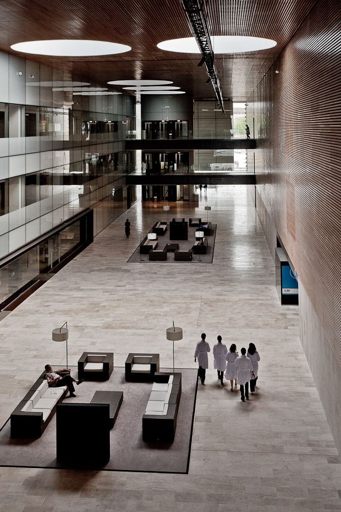 Fotografía del interior de un hospital con un gran atrio cubierto por cuya parte inferior camina un grupo de médicos