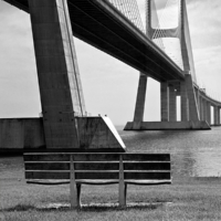Vista en blanco y negro del puente desde la orilla norte, con un banco en primer plano.
