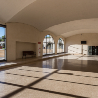 Interior de la zona de taquillas con sombras contrastadas por la luz de atardecer que se cuela por los ventanales.