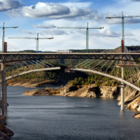 Viaducto en construcci&oacute;n, con distintas gr&uacute;as, sobre un embalse con baja capacidad.