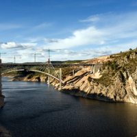 Viaducto en construcci&oacute;n, con distintas gr&uacute;as, sobre un embalse con baja capacidad.