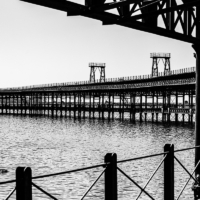 Imagen en blanco y negro en la que la silueta del muelle recorre la foto en curva.