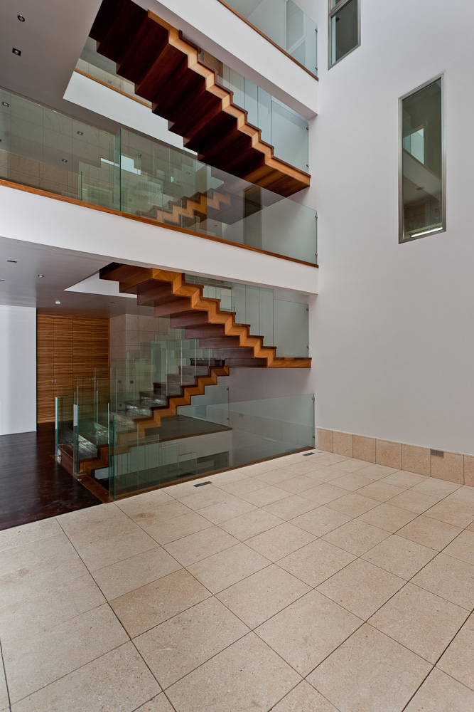 Fotografía vertical de un luminoso atrio donde destacan unas escaleras paneladas en madera y con barandilla de cristal