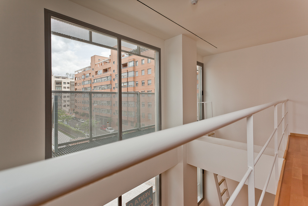 Fotografía desde la planta superior de un loft con grandes ventanales y paredes blancas