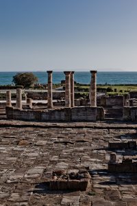 Fotografía con vistas al mar de parte de las ruinas donde sobresalen unas columnas que, al coincidir con la línea de horizonte, parecen sujetar el cielo.